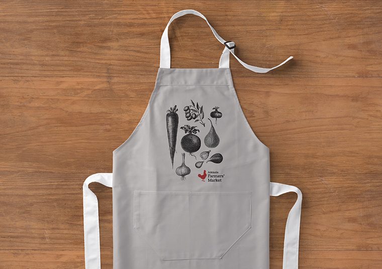 Apron lying on the floor with Adelaide Showground Farmers' Market logo and images of fruit and vegetables printed on