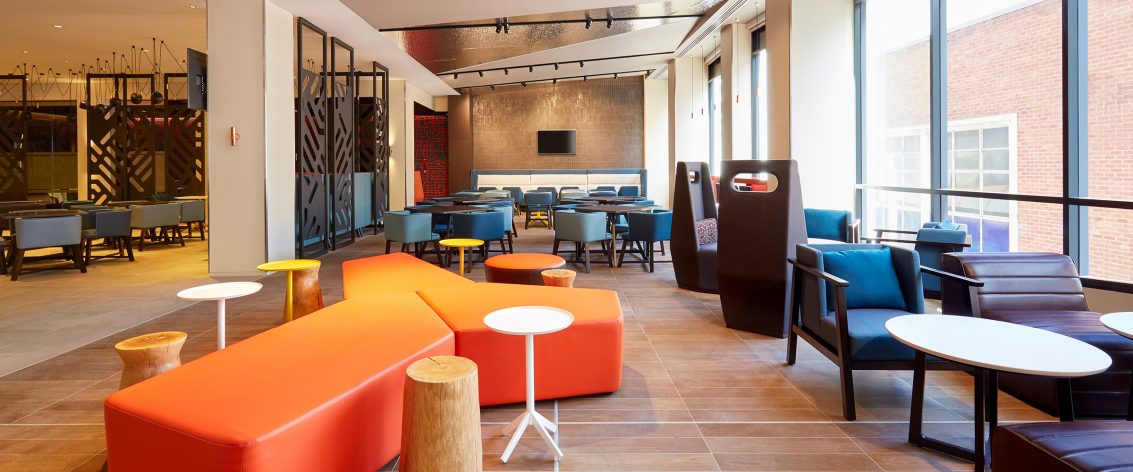Room filled with a bright orange lounge and many stools and chairs